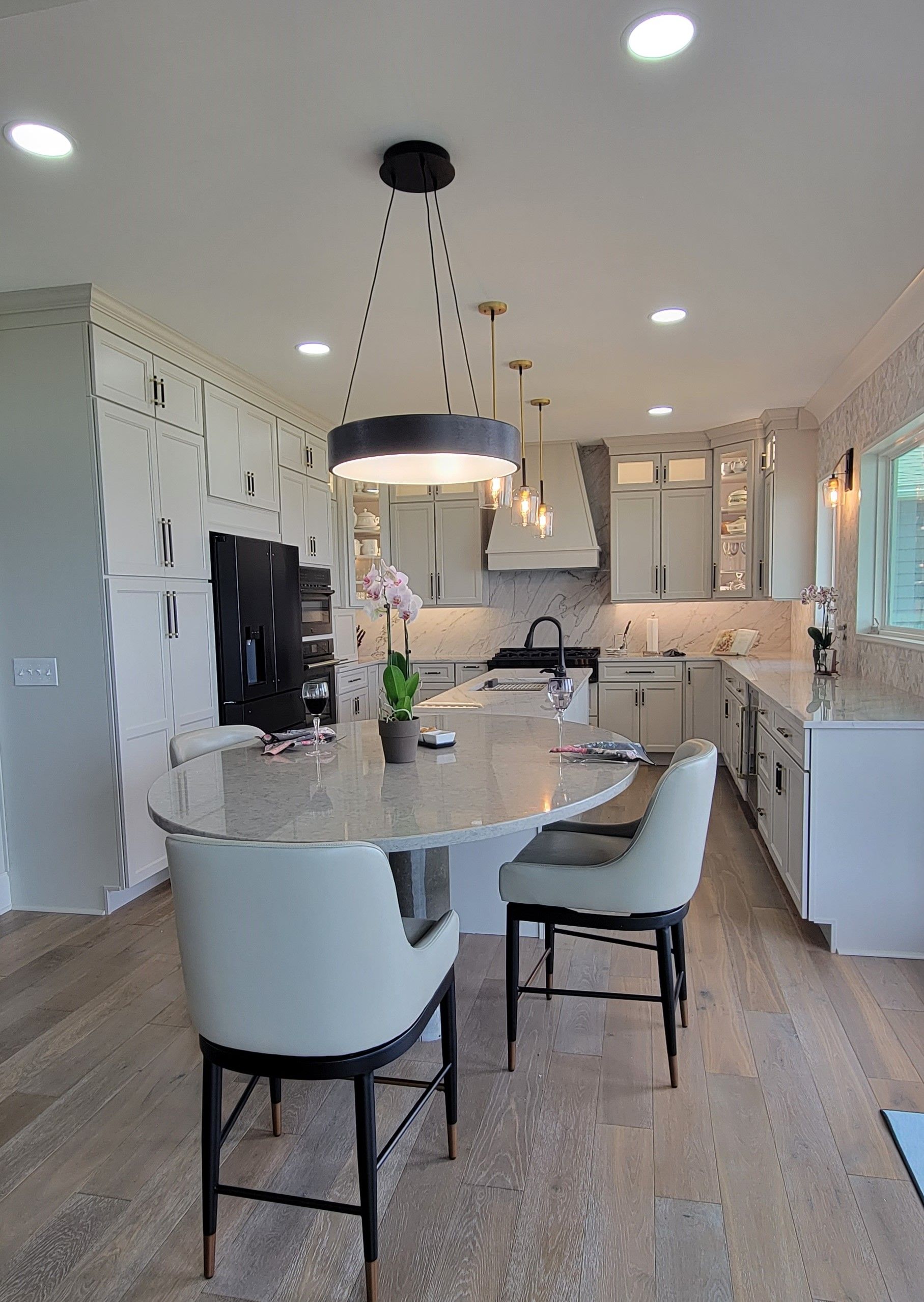 Modern kitchen with island, pendant lights, two bar stools, light cabinets, and wood flooring.