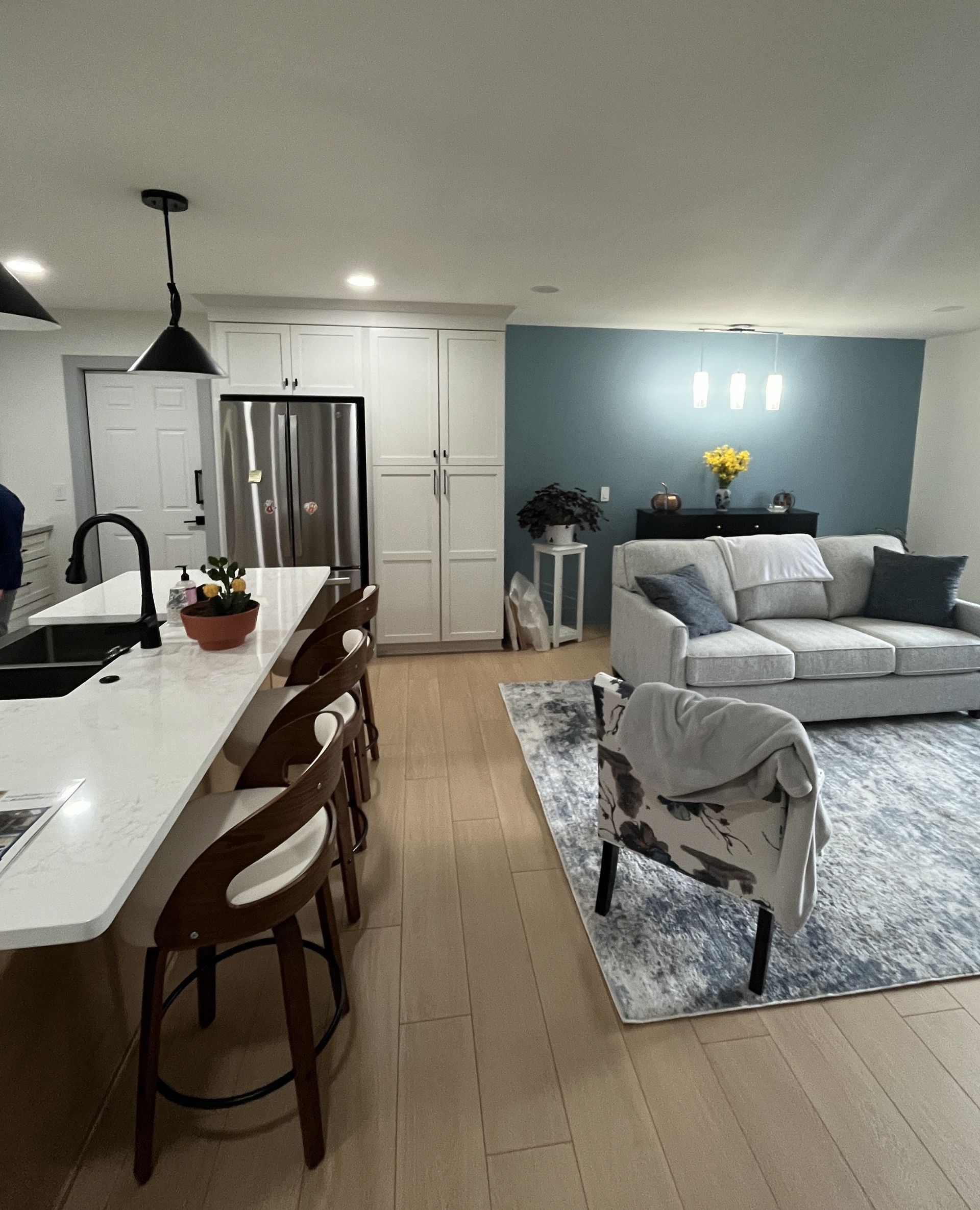 Open-concept kitchen and living room. Kitchen island with stools, white cabinets, and blue accent wall.