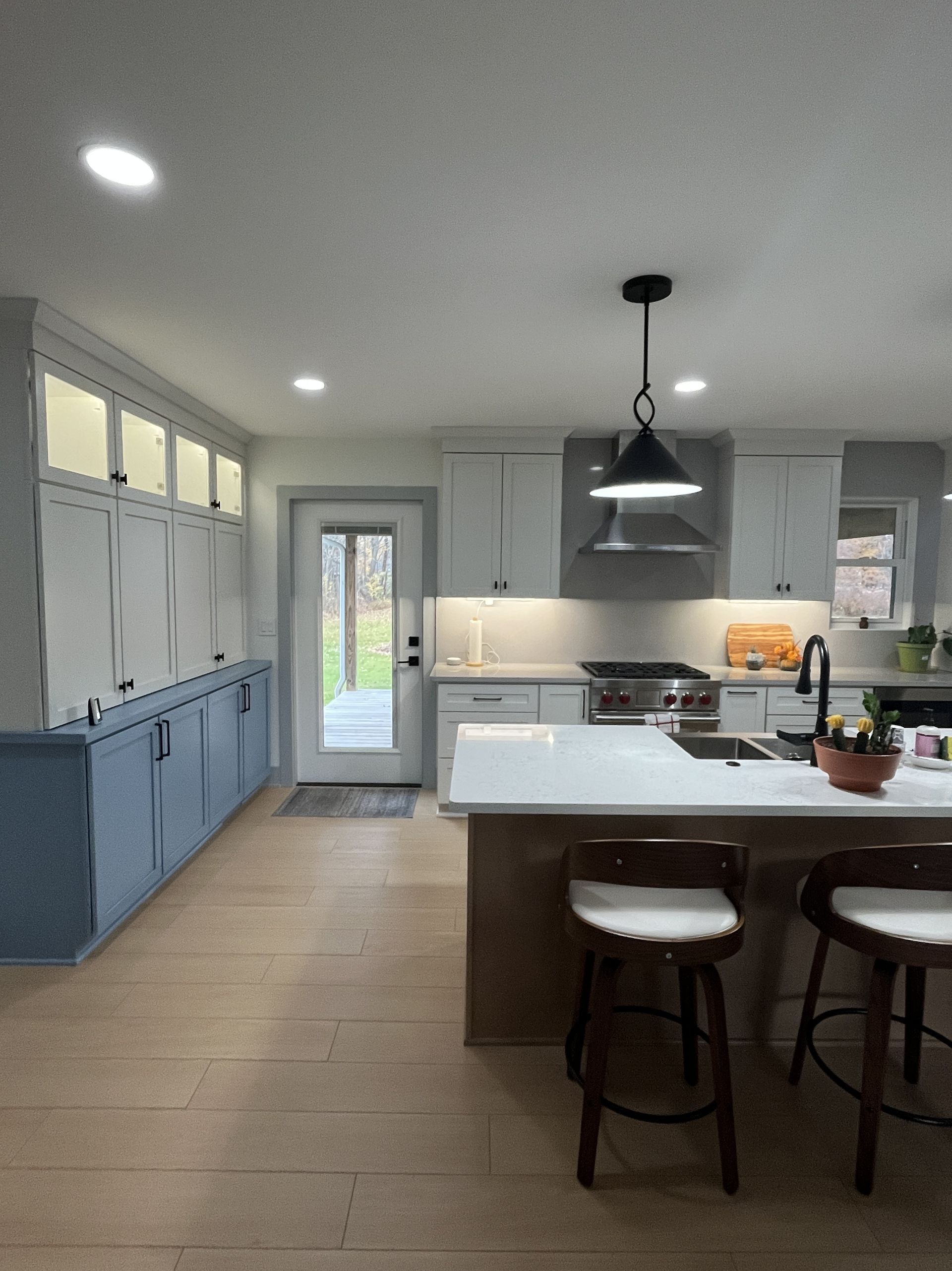 Modern kitchen with light wood floor, white and blue cabinets, island with stools.