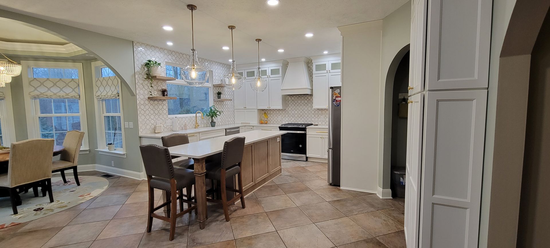 Spacious kitchen with island seating, pendant lights, tile backsplash, and a dining area visible through an archway.
