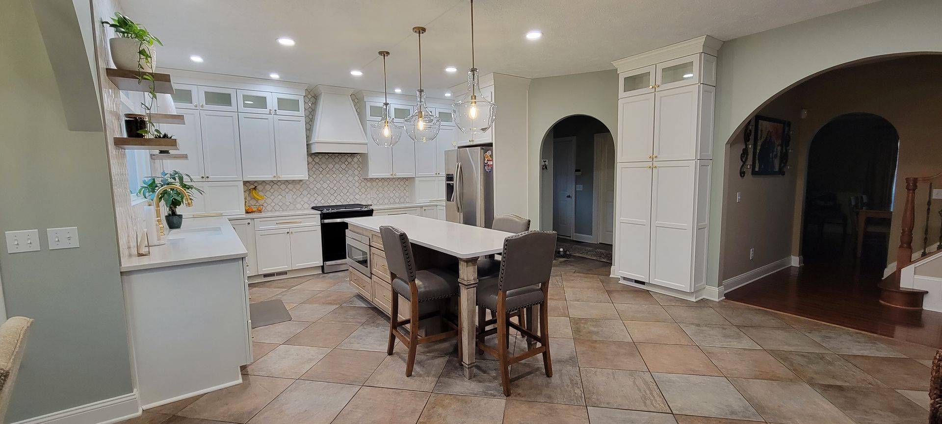 Kitchen with white cabinets, island with stools, and stone tile floor.