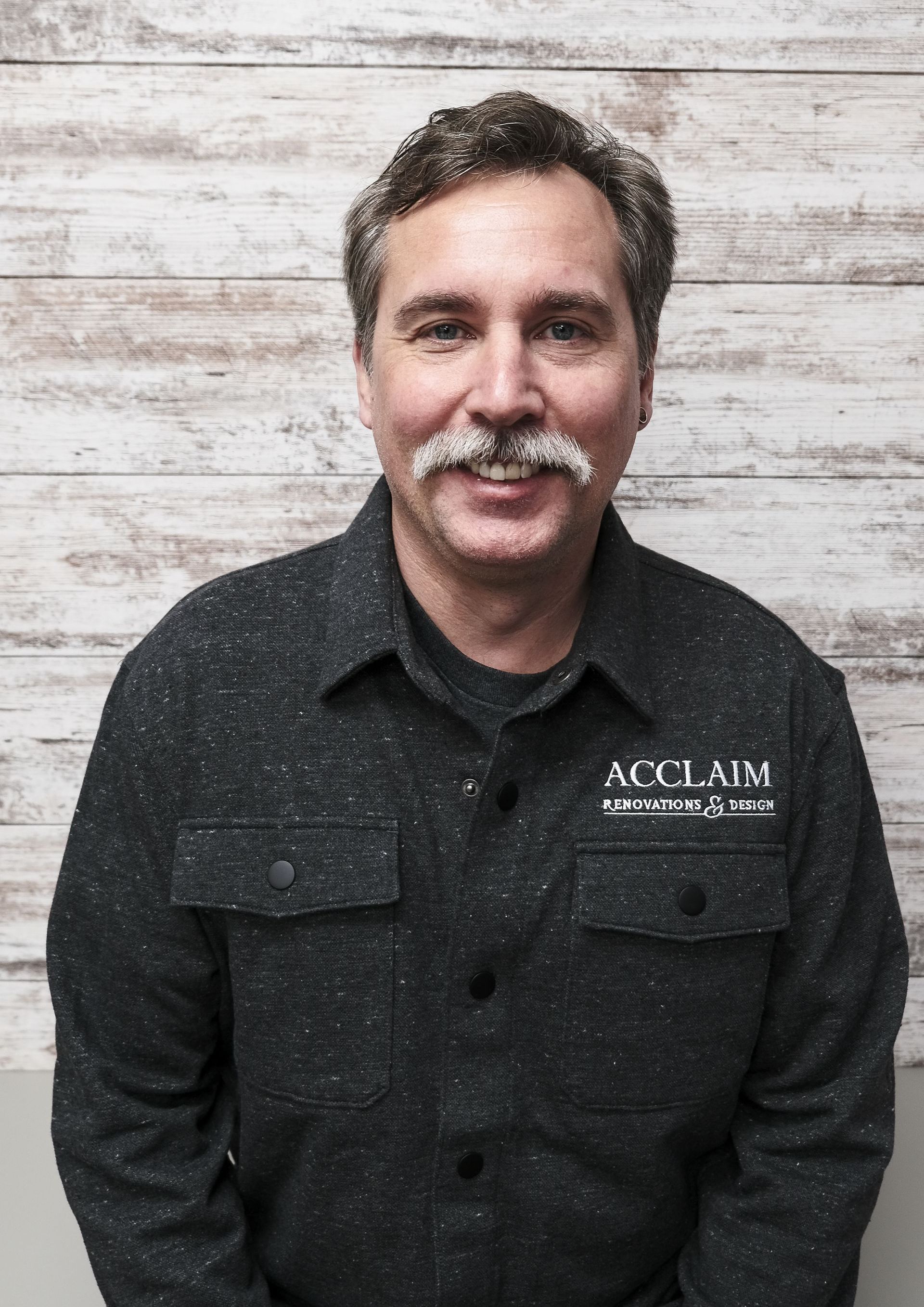Man with a mustache wearing a black shirt with the logo 
