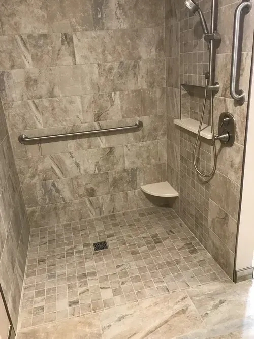 Accessible shower with grab bars and built-in shelves. Beige tile covers walls and floor.