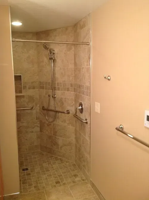 Accessible shower stall with grab bars and tiled walls and floor.