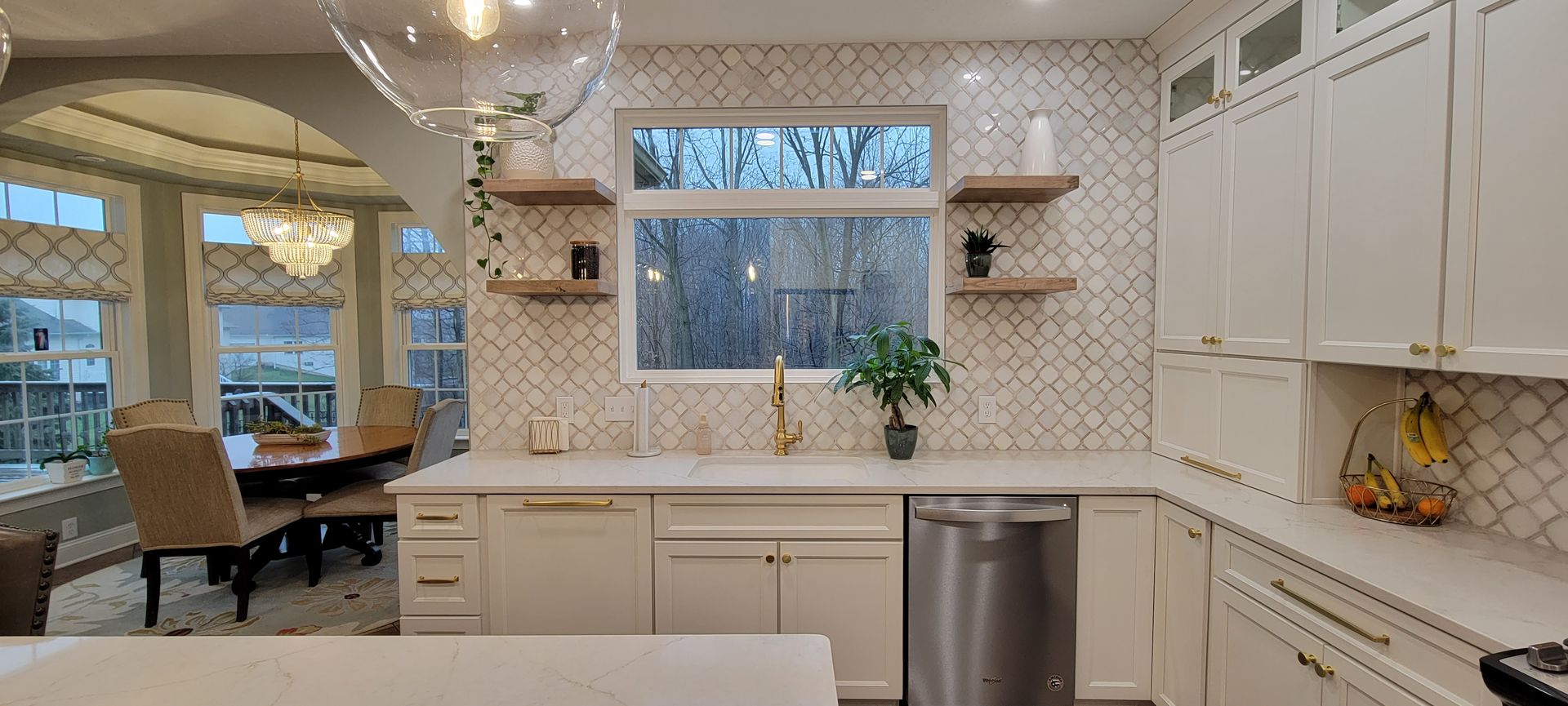 Modern white kitchen with gold hardware and a view of trees from the window.