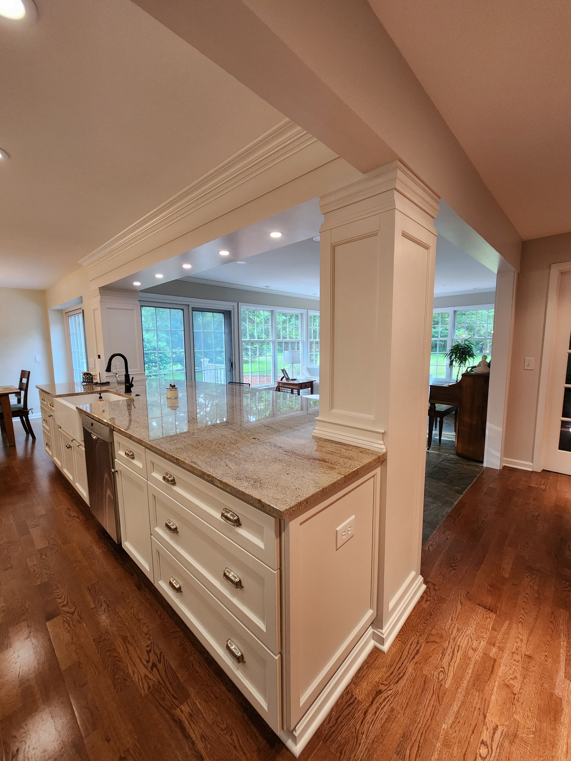 Kitchen with white cabinets, granite countertop, and wood floors. Sunlight streams through windows.