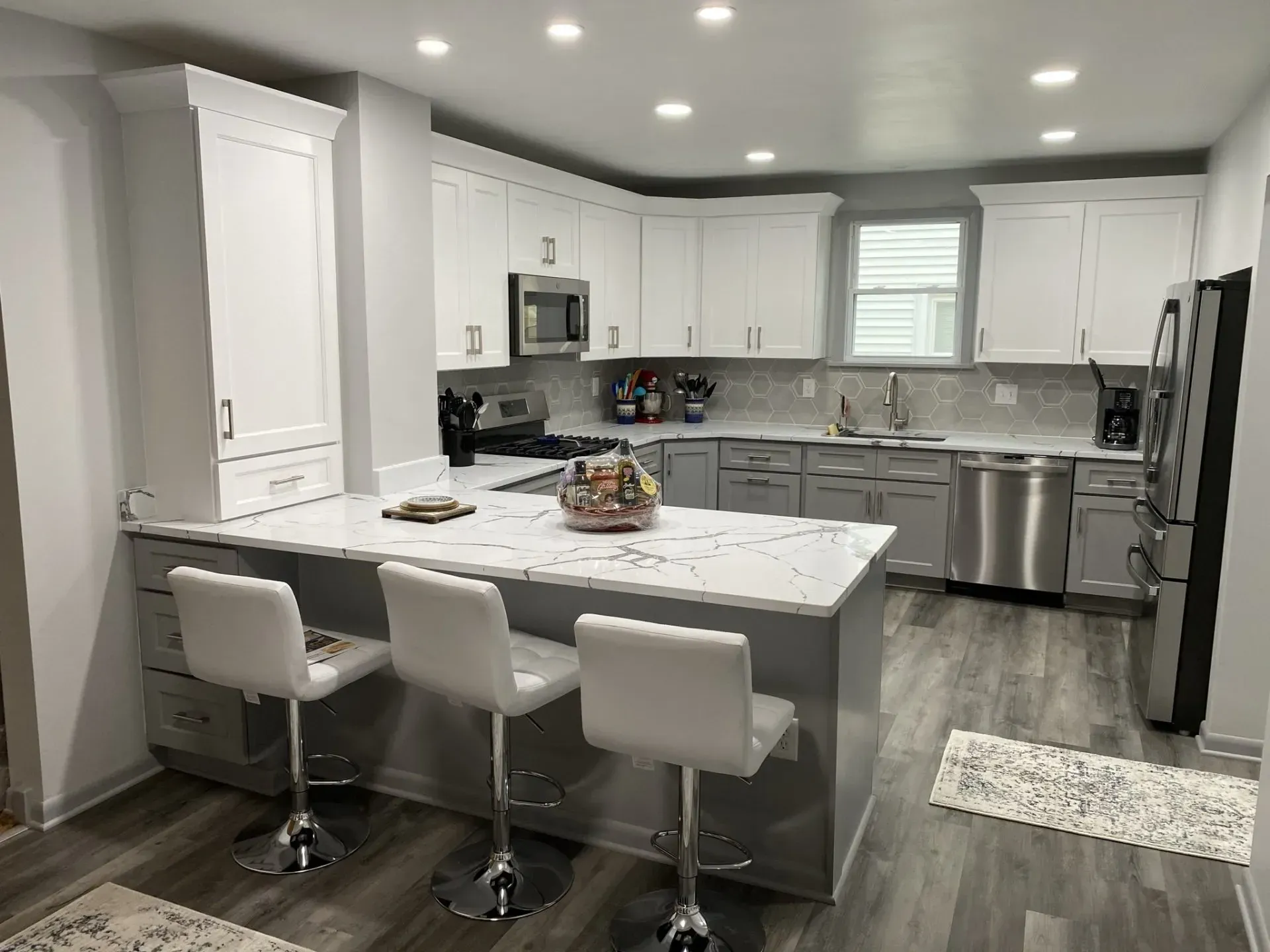 Modern kitchen with gray and white cabinets, stainless steel appliances, and a breakfast bar with three stools.