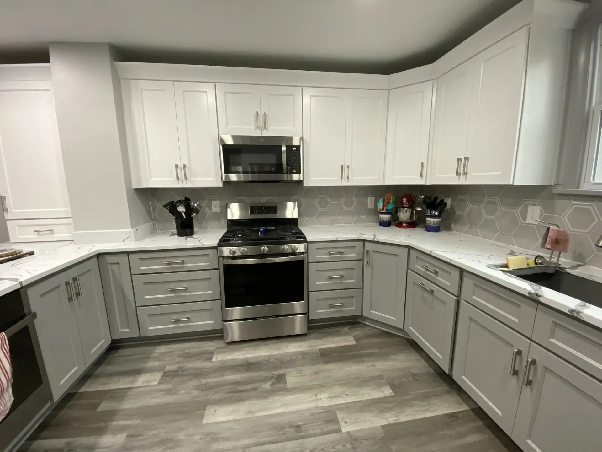 Modern kitchen with white and gray cabinets, stainless steel appliances, and a gray patterned backsplash.