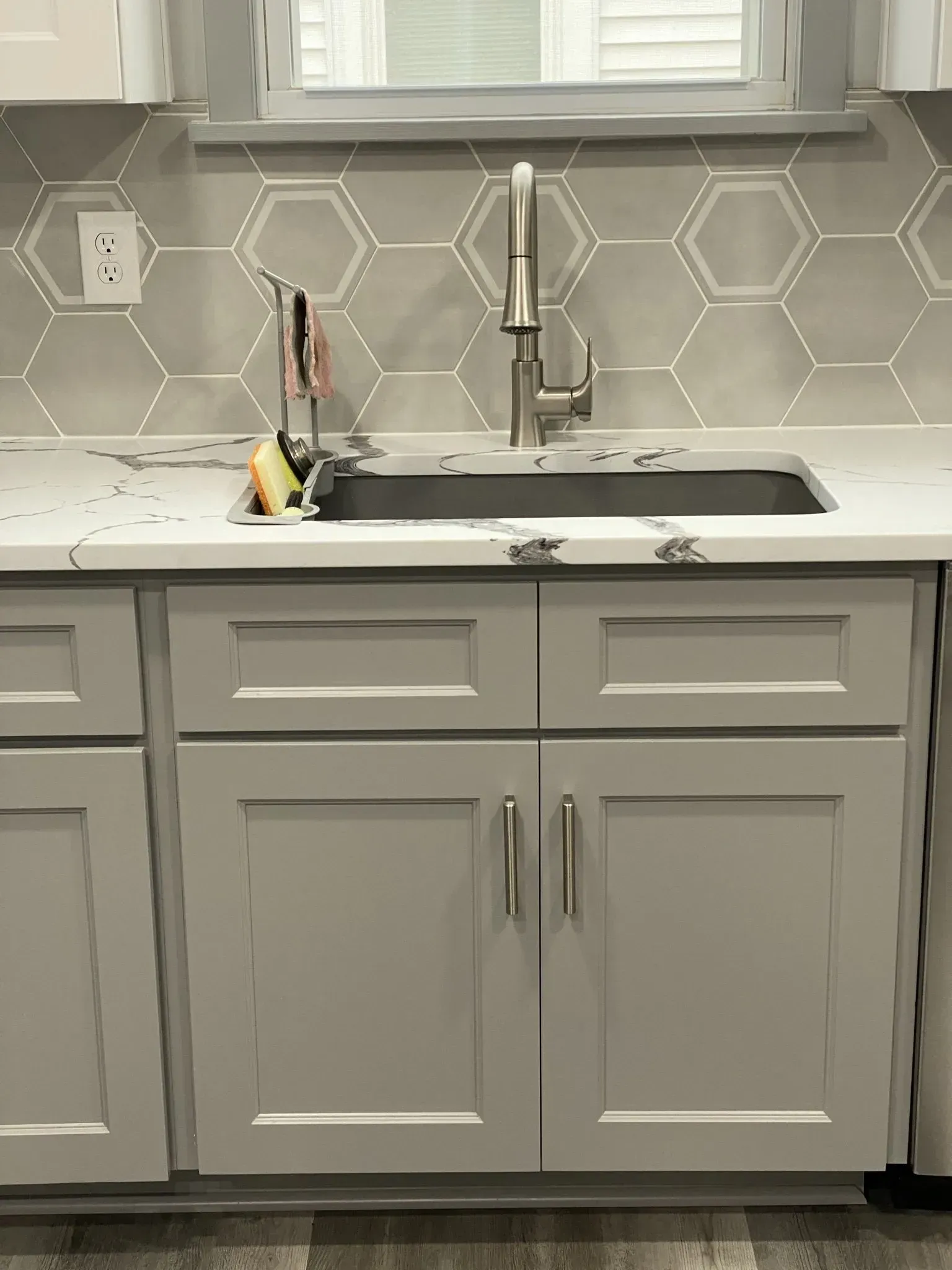 Gray kitchen cabinets with a sink, faucet, and hexagon tile backsplash.