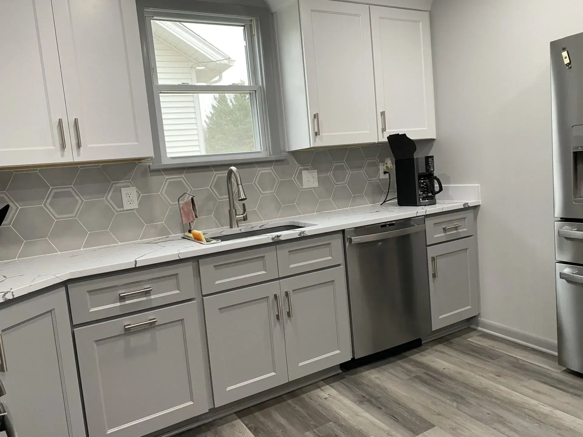 Modern kitchen with gray cabinets, white countertops, stainless steel appliances, and hexagon tile backsplash.