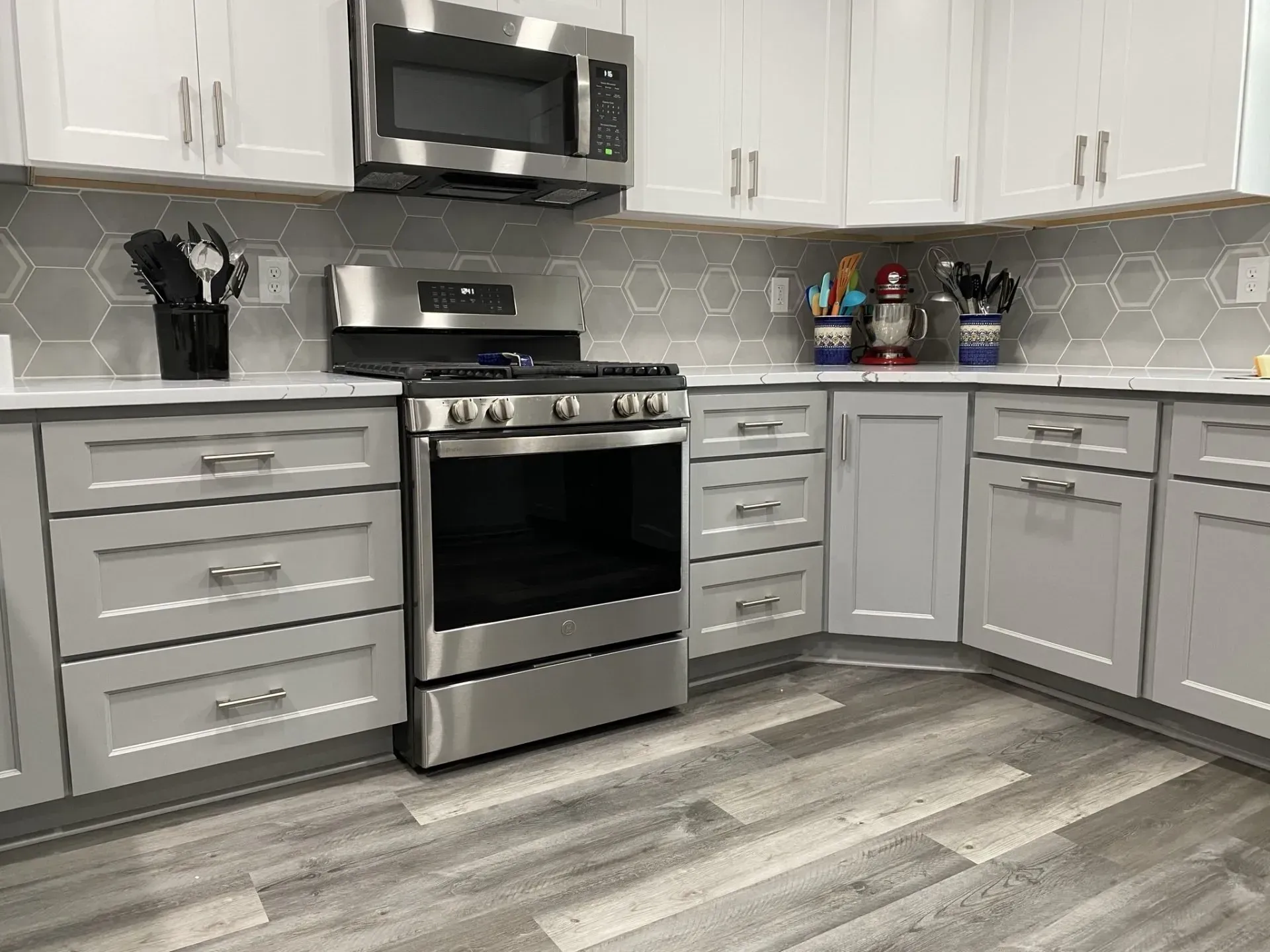 Modern kitchen with gray and white cabinets, stainless steel appliances, and hexagon tile backsplash.