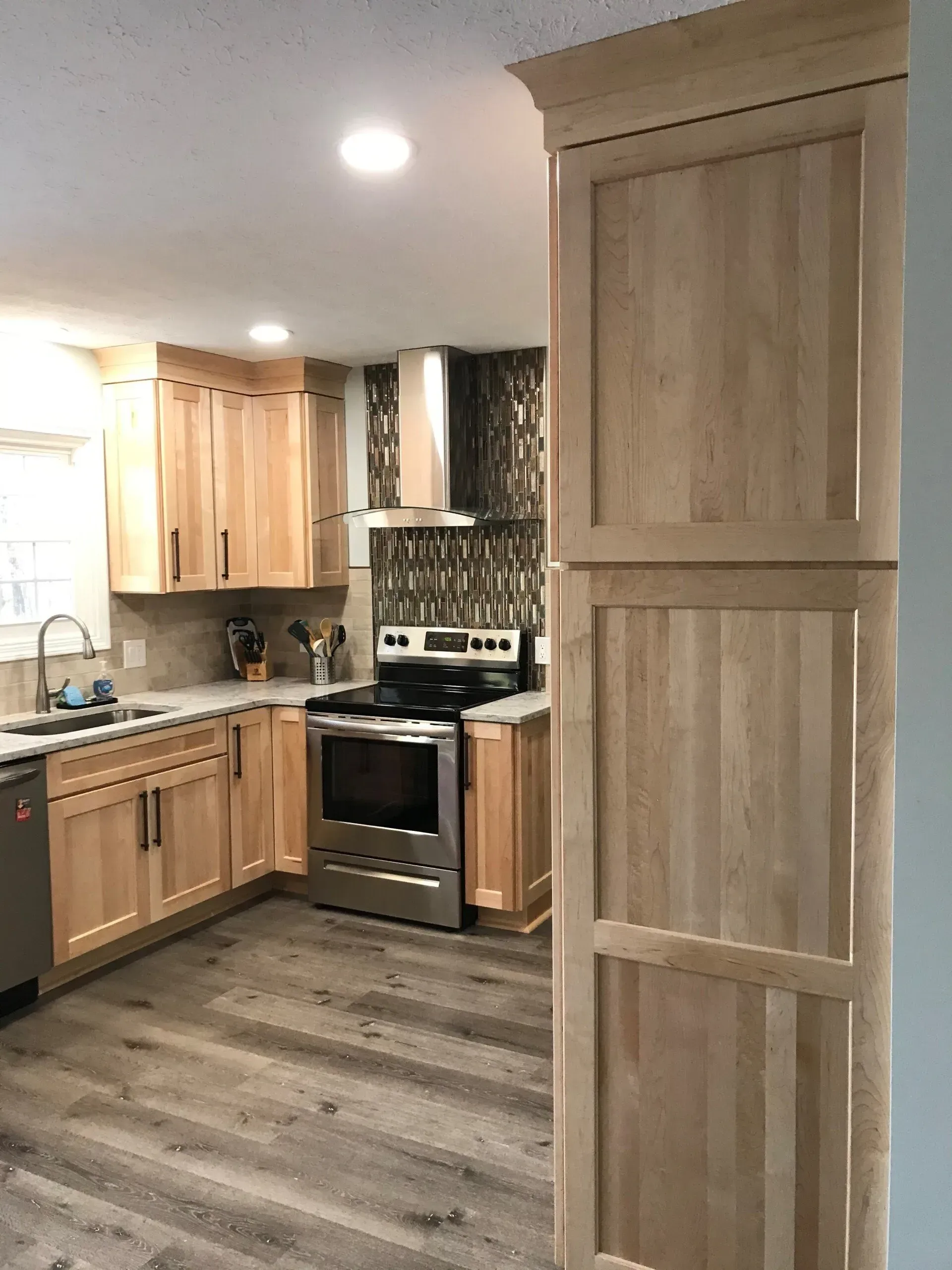 Kitchen with light wood cabinets, stainless steel appliances, and gray flooring.