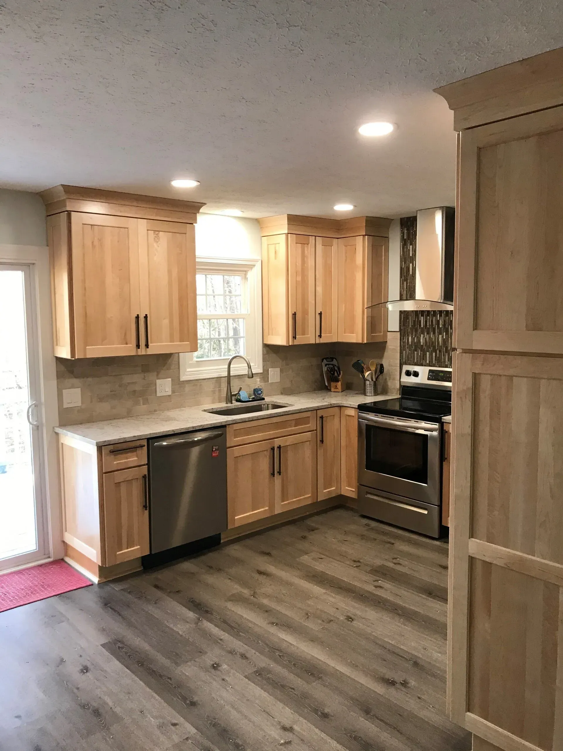 Kitchen with light wood cabinets, stainless steel appliances, and gray flooring.