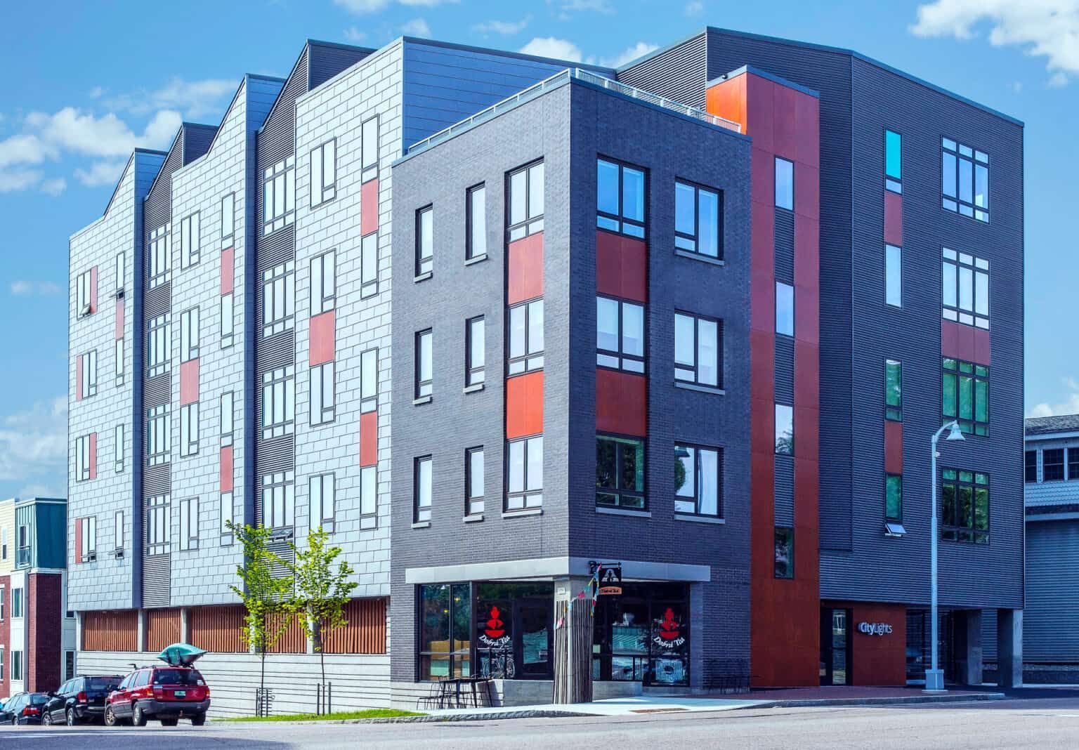 A large building with a lot of windows is sitting on the corner of a city street.