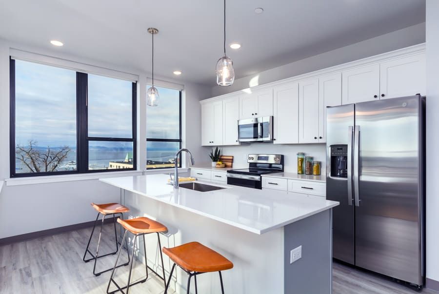 A kitchen with white cabinets , stainless steel appliances , a refrigerator and a large island.