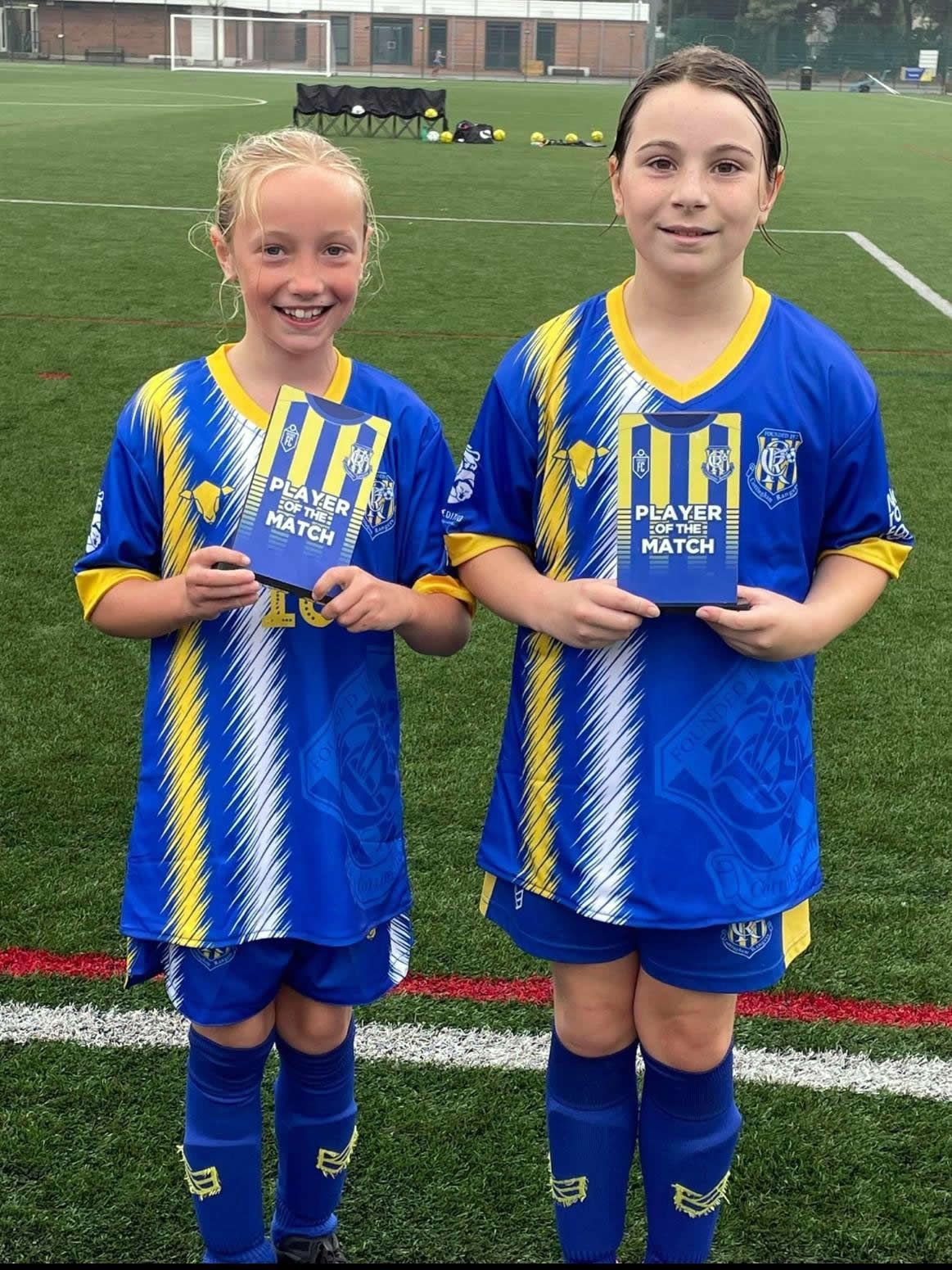Two girls in blue soccer uniforms holding