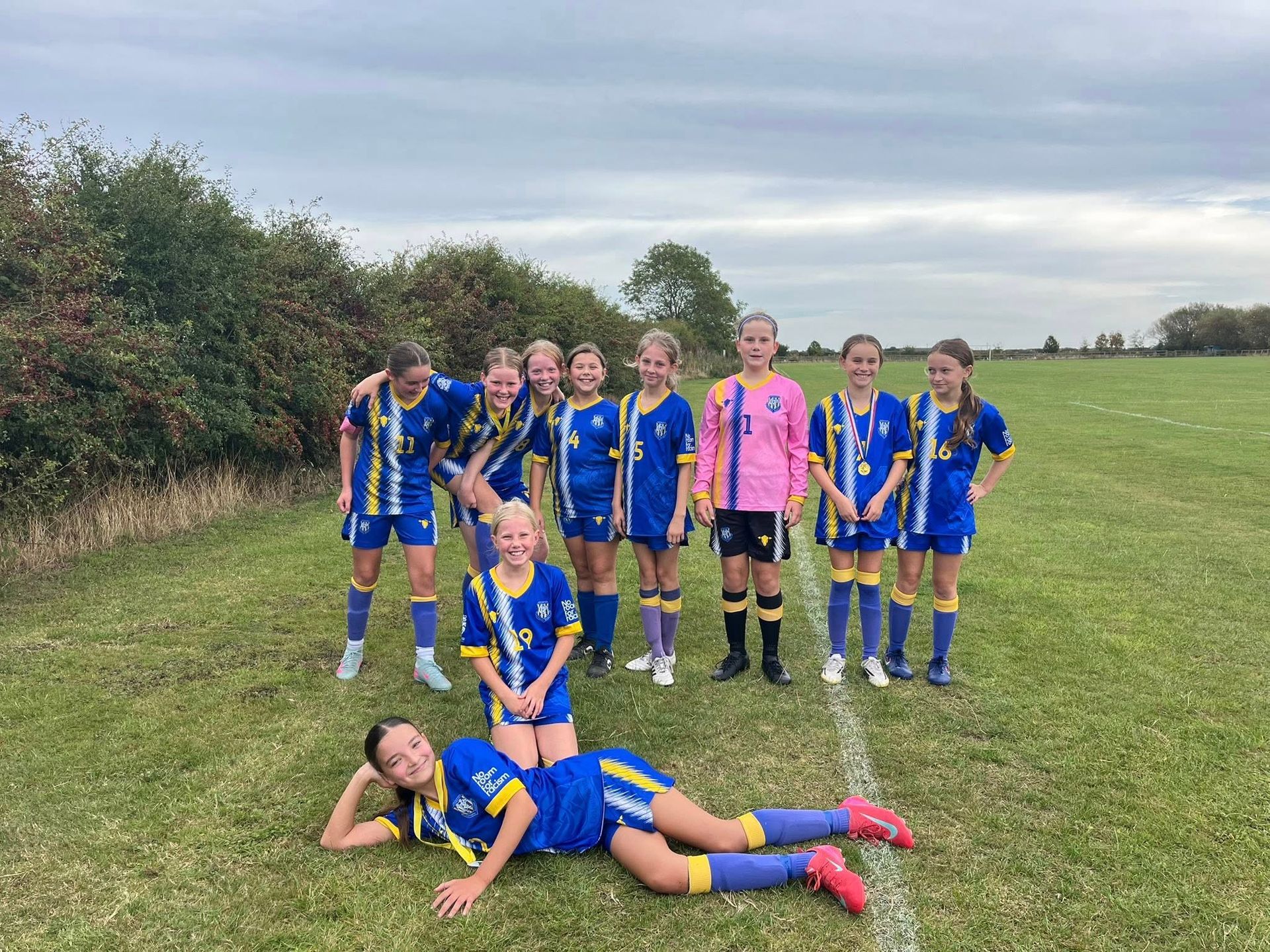 Youth soccer team in blue and yellow uniforms poses on a field, one player lies down.