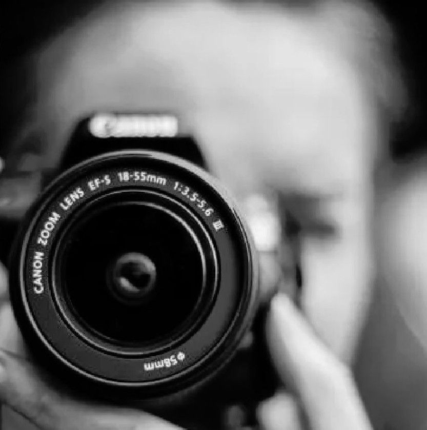 Person holding a Canon camera, focusing lens, close-up, black and white.