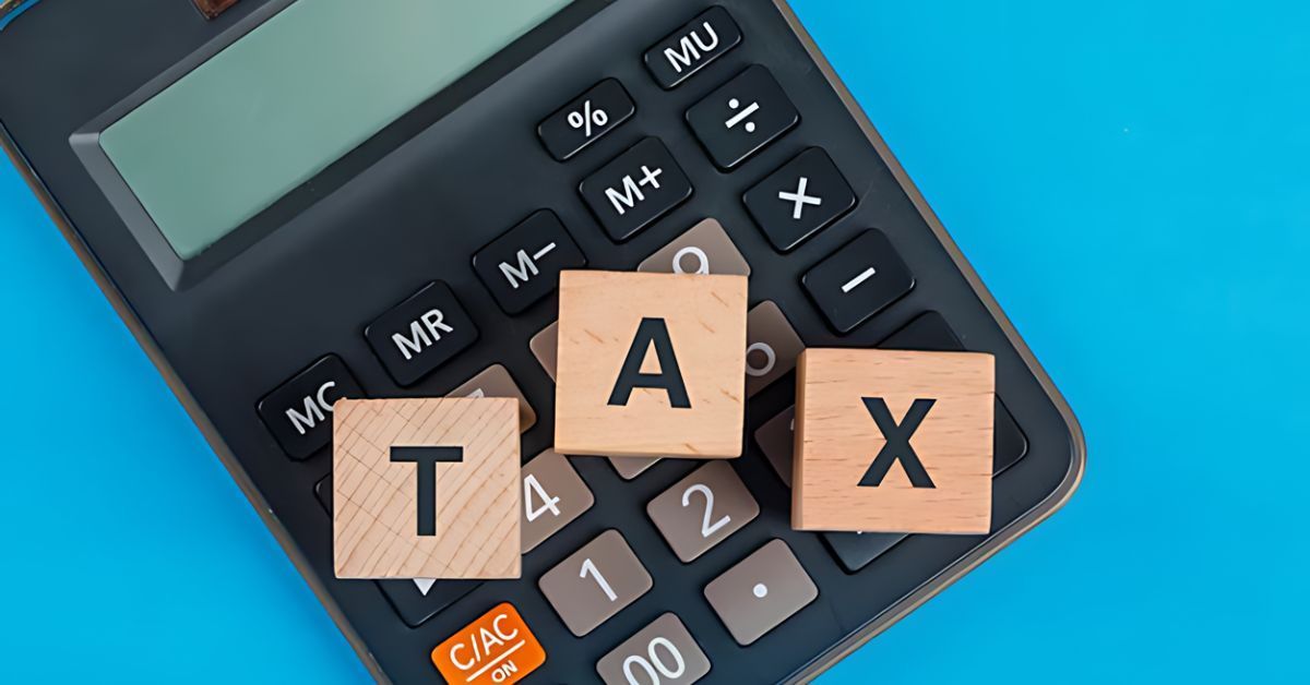 Calculator with wooden letter tiles spelling “TAX” on a blue background