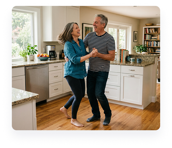 Two people dancing in a bright kitchen, smiling and holding hands.
