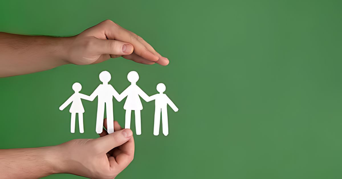 Hands sheltering paper cutout family on green background