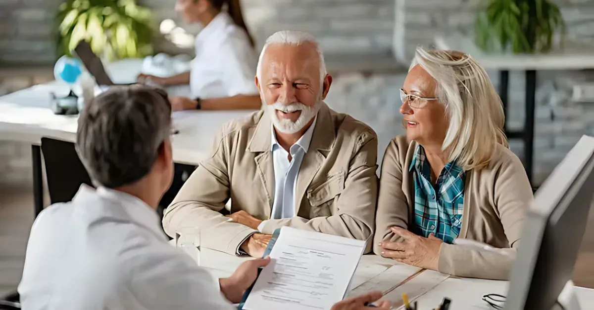 Three people in a meeting, smiling and reviewing documents at a table in a bright office