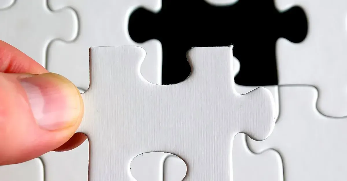 Hand placing a white puzzle piece among interlocking white and black pieces