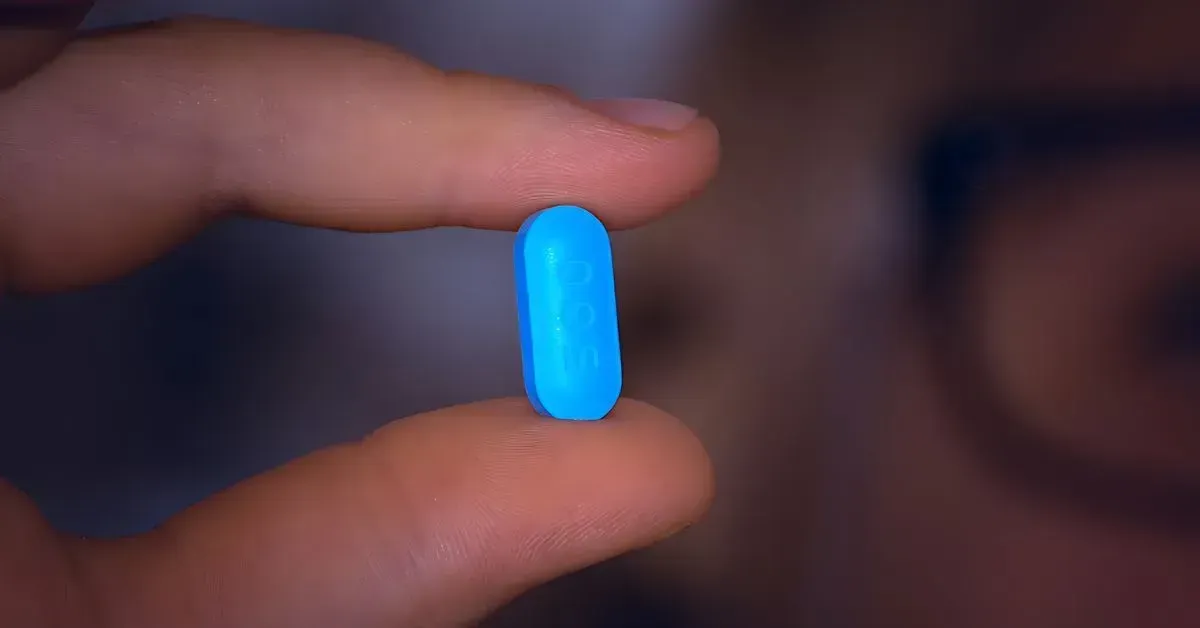 A hand holding a small glowing blue capsule-like object against a blurred background