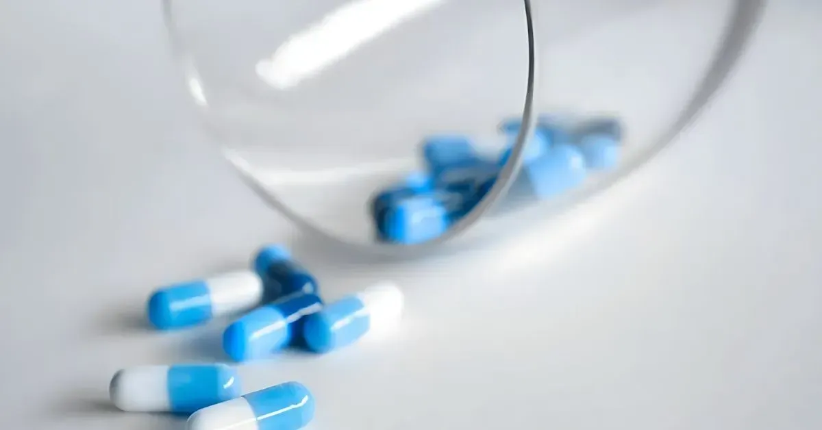 Blue and white capsules scattered beside a magnifying glass on a white surface