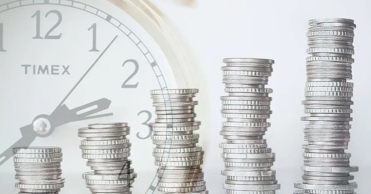 Clocks behind stacks of coins rising in height, symbolizing savings and financial growth