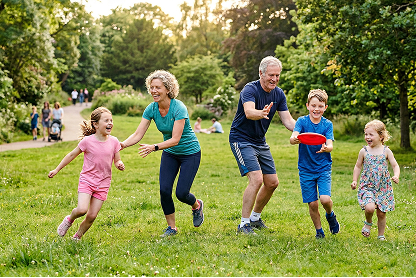 Family playing and laughing together in a sunny park, holding hands on the grass.