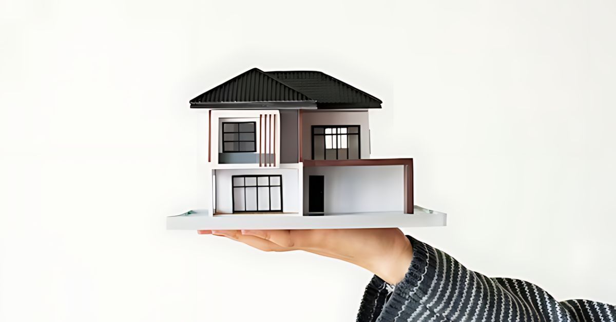 Hand holding a small modern house model against a white background