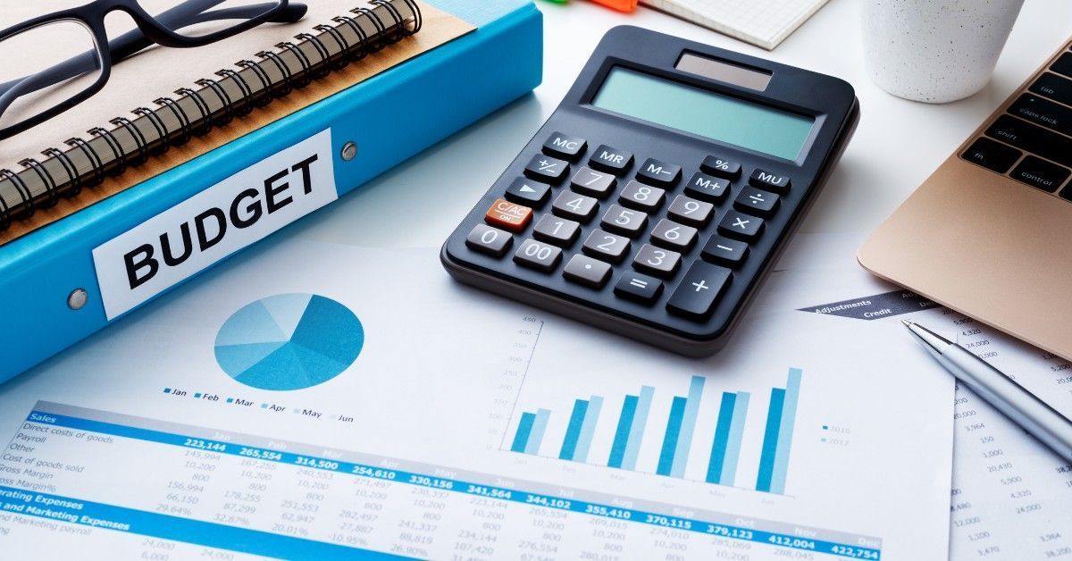 Budget spreadsheet with calculator, charts, and blue binder on a desk