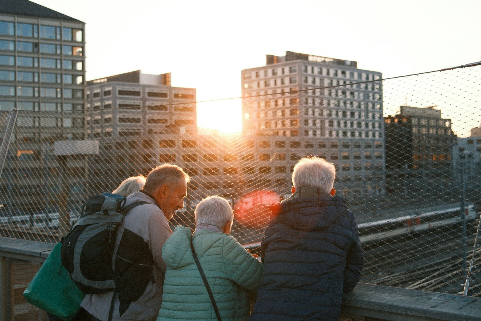 Three people stand on a bridge at sunset, looking over city buildings.