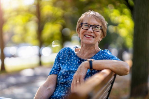 Smiling woman with glasses resting on a chair in a sunlit park