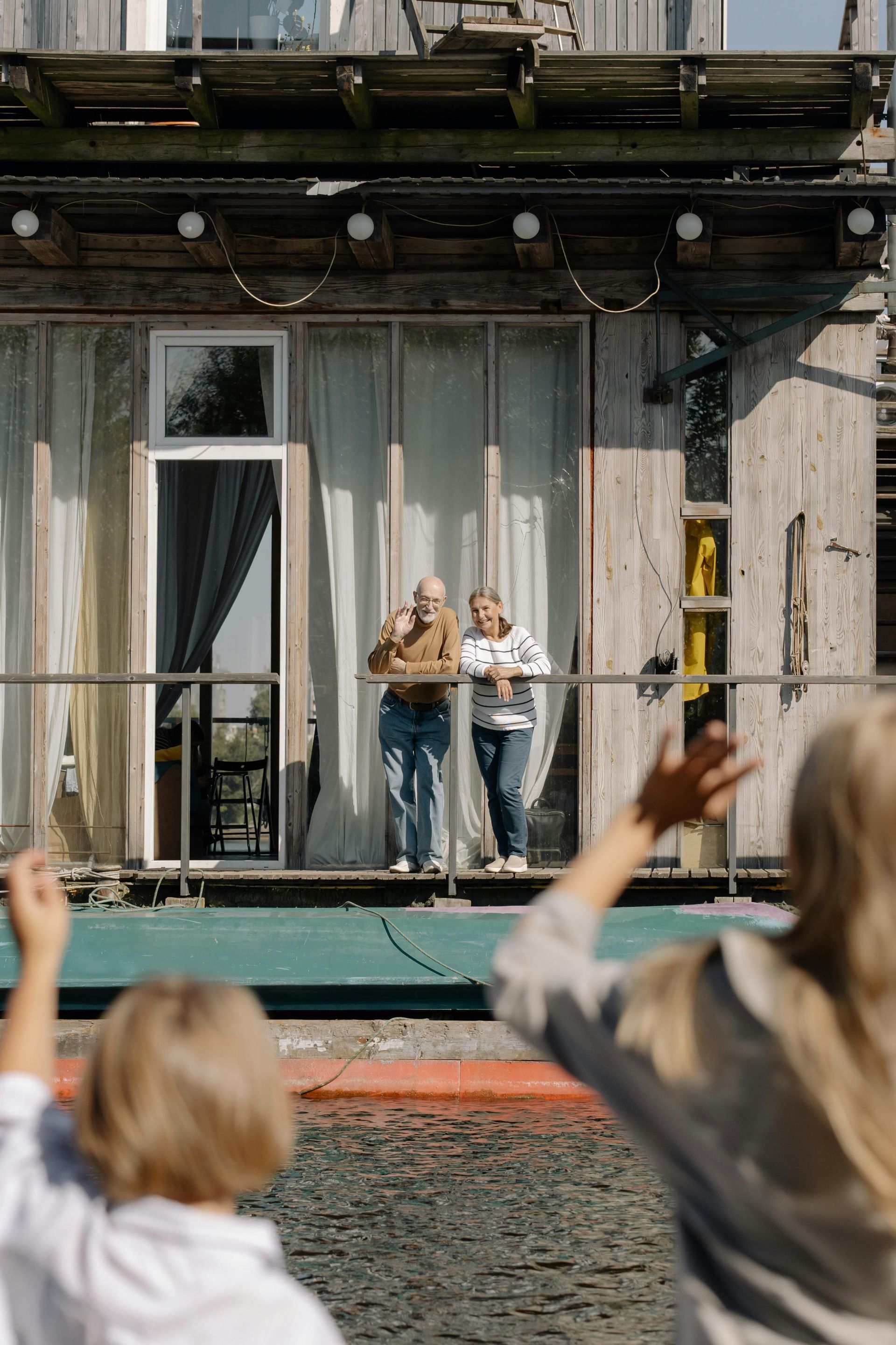 Two people standing on a balcony above water, with a crowd watching from below.
