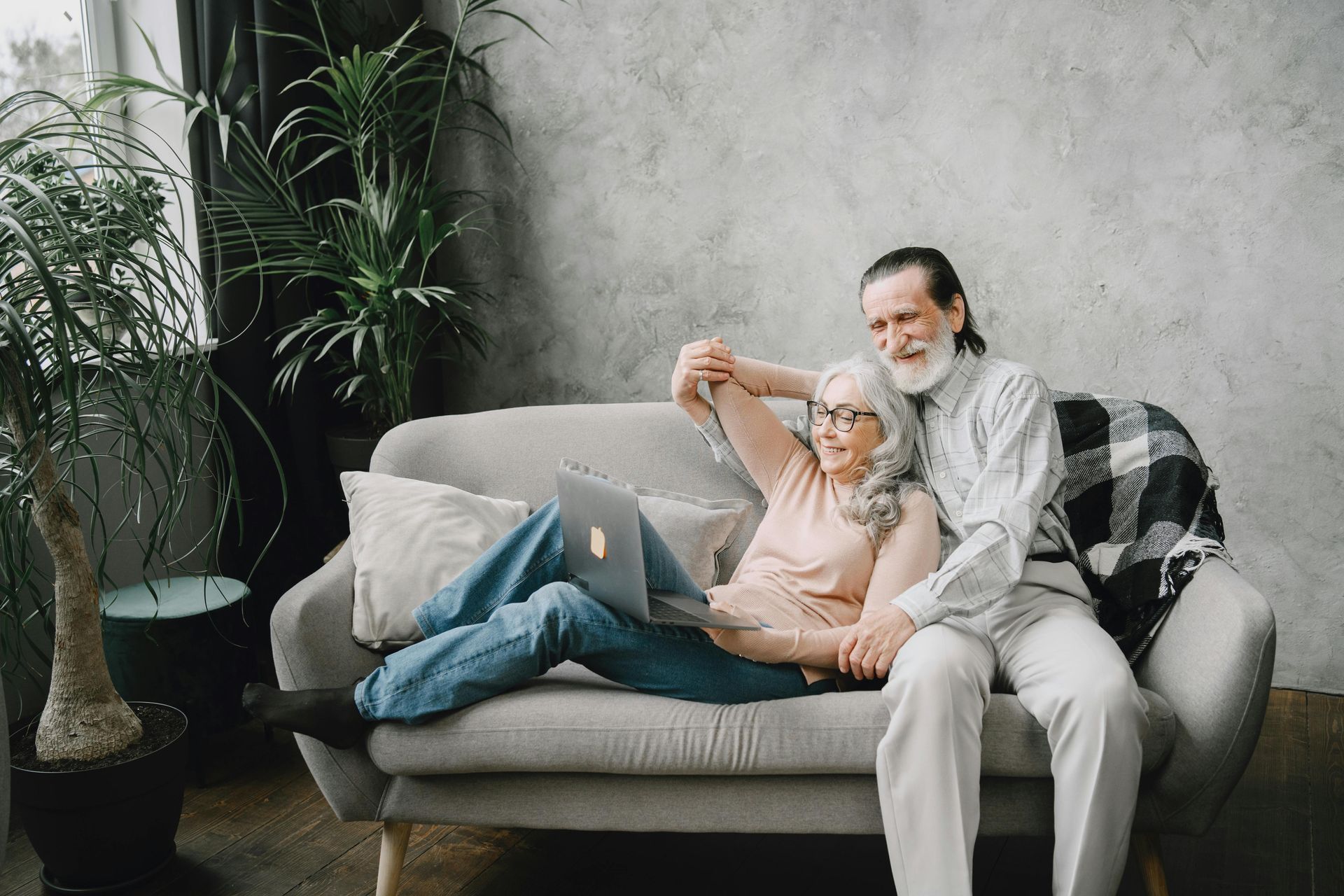 Person relaxing on a sofa with a laptop, stretching beside a potted plant in a cozy living room