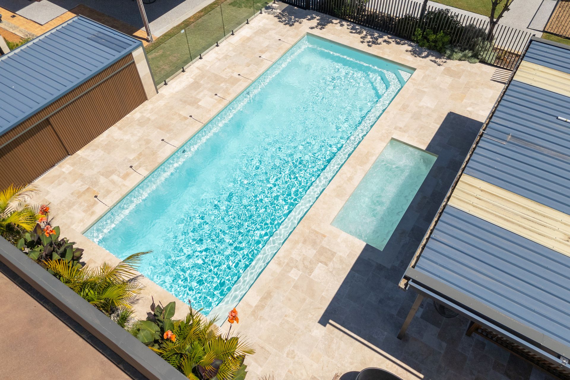 A Large Swimming Pool is Surrounded by a Fence and Trees — Gibson Family Pools Pty Ltd In Port Macquarie, NSW