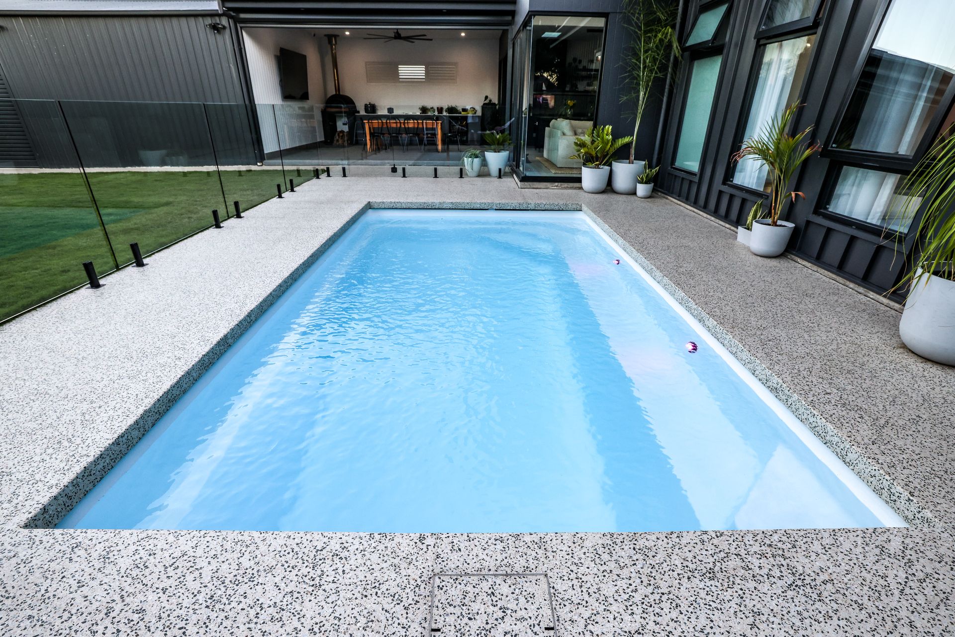 A Man is Cleaning a Swimming Pool With a Broom — Gibson Family Pools Pty Ltd In Forster, NSW