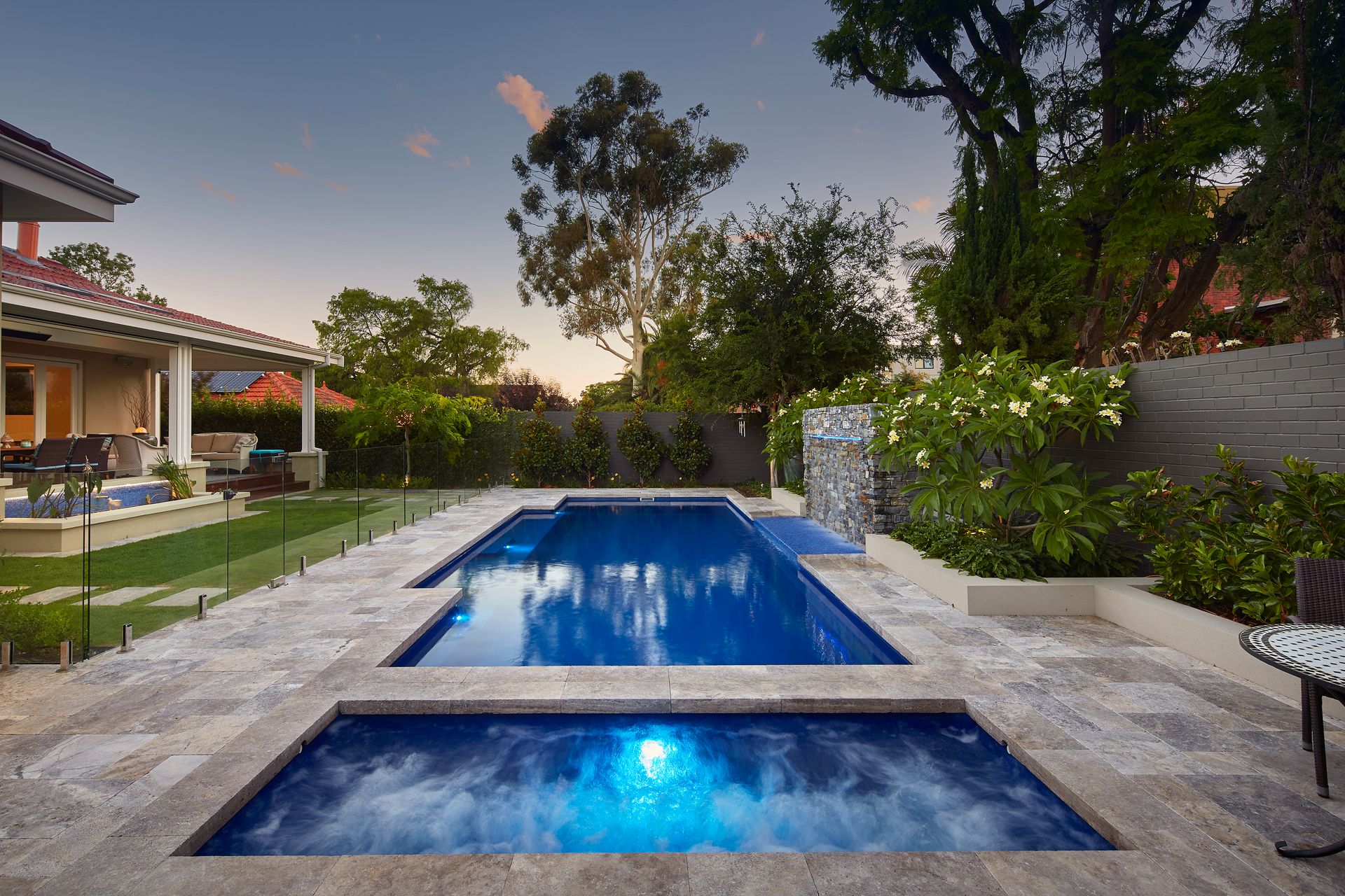 A Small Swimming Pool is Surrounded by a Glass Fence and a Wooden Deck — Gibson Family Pools Pty Ltd In Harrington, NSW