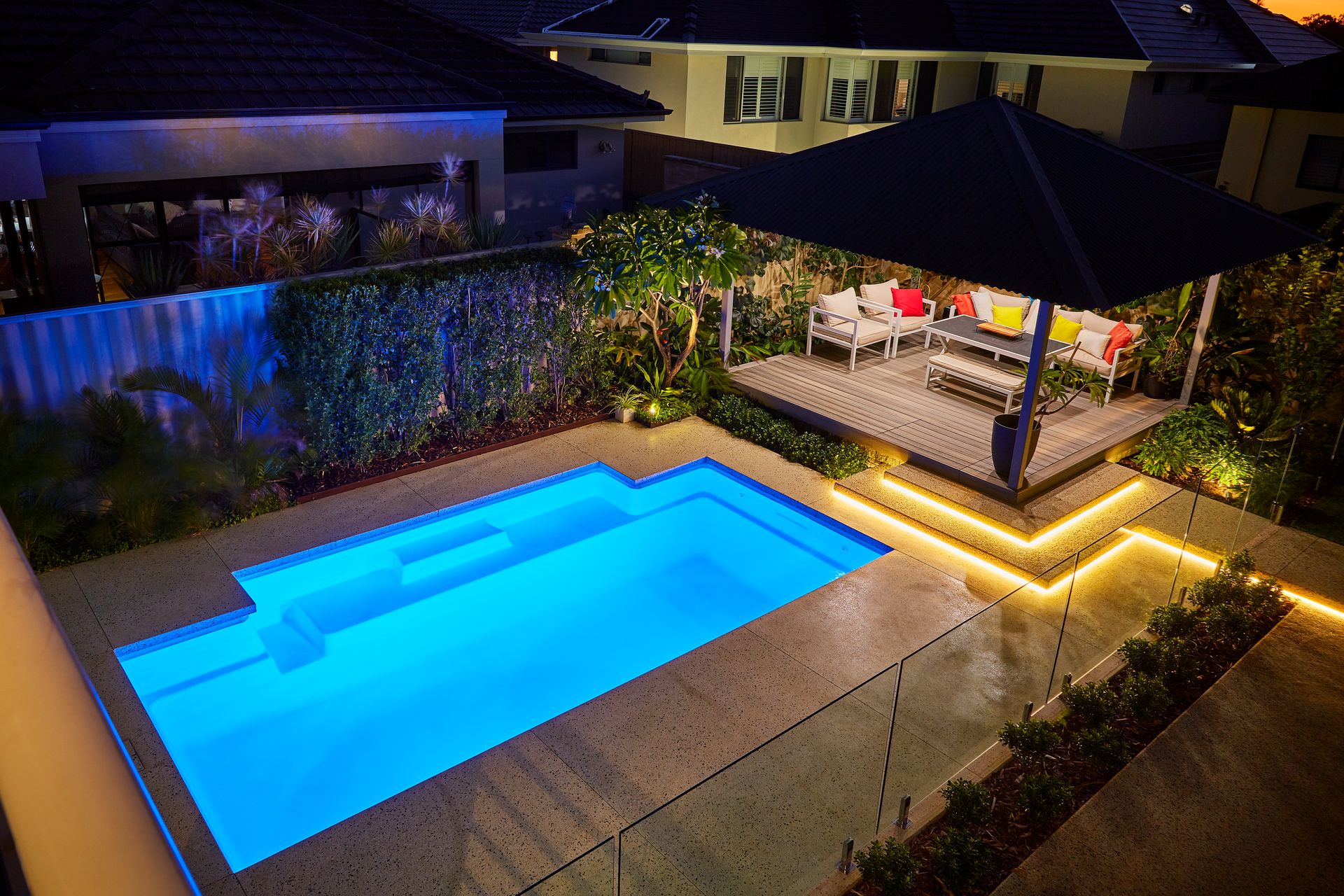A Small Swimming Pool is Surrounded by a Glass Fence and a Wooden Deck — Gibson Family Pools Pty Ltd In Port Macquarie, NSW