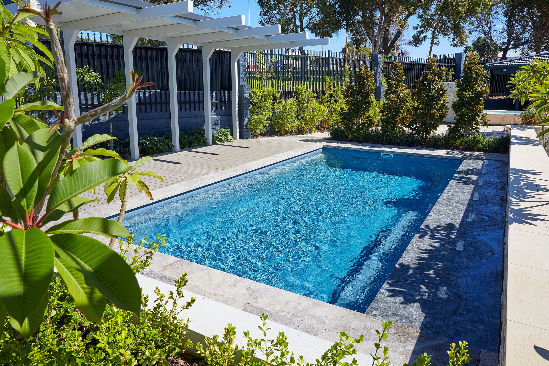 A Small Swimming Pool is Surrounded by a Glass Fence and a Wooden Deck — Gibson Family Pools Pty Ltd In Wauchope, NSW