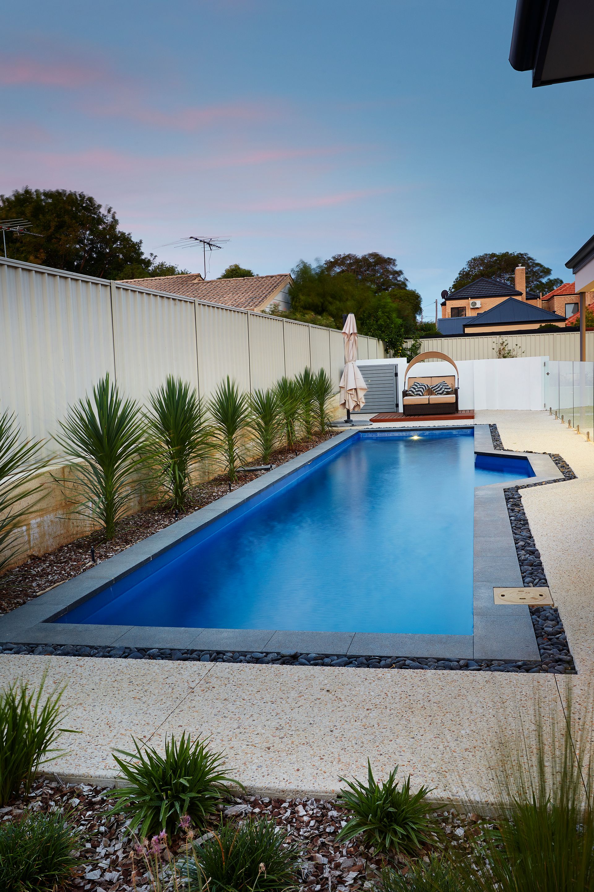 A Large Swimming Pool is Surrounded by a Fence and Trees — Gibson Family Pools Pty Ltd In Port Macquarie, NSW