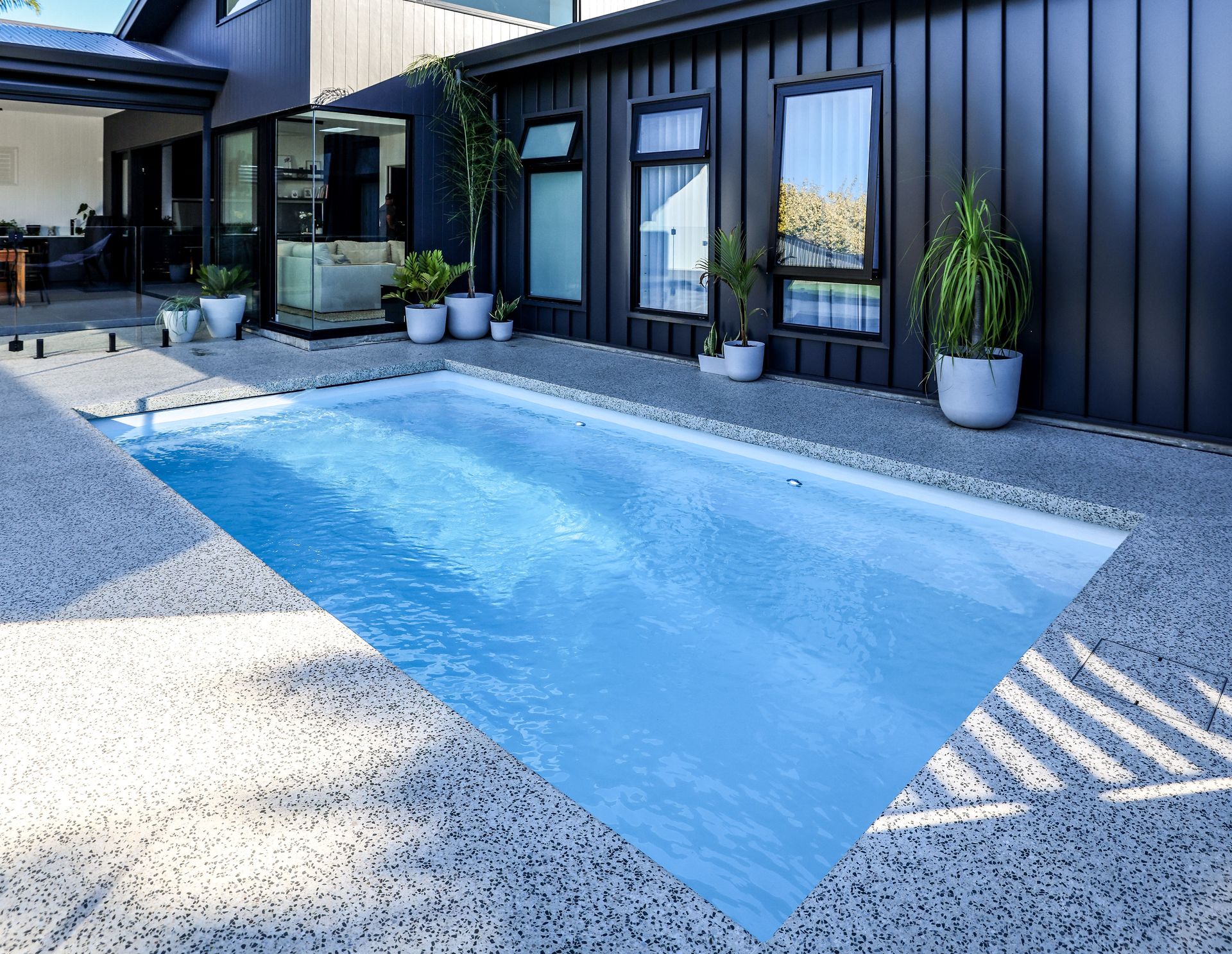 A Large Swimming Pool is Surrounded by a Fence and Trees — Gibson Family Pools Pty Ltd In Wauchope, NSW