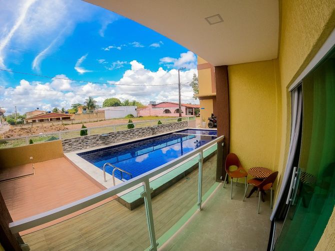Prédio de apartamentos amarelo com varanda e piscina azul sob um céu parcialmente nublado.
