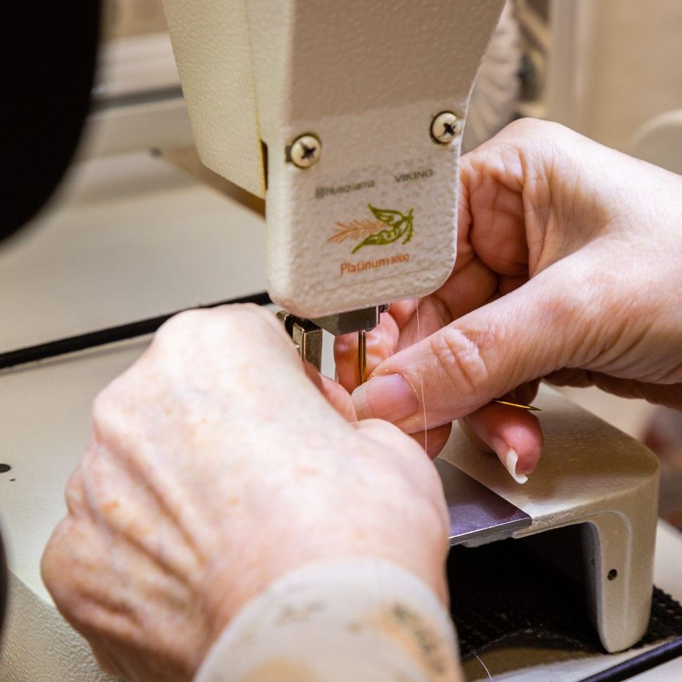 Hands guiding fabric under a sewing machine needle at workbench