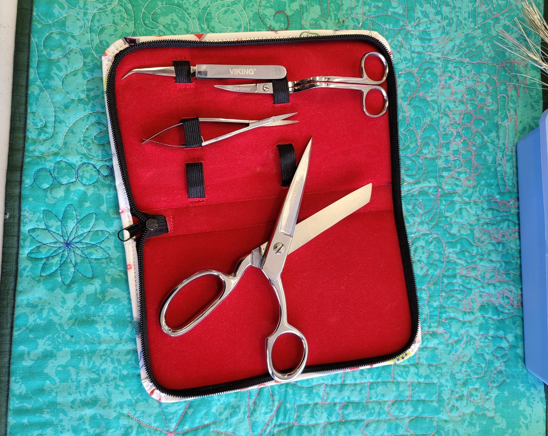 Open red case with silver grooming scissors and combs on a turquoise textured surface