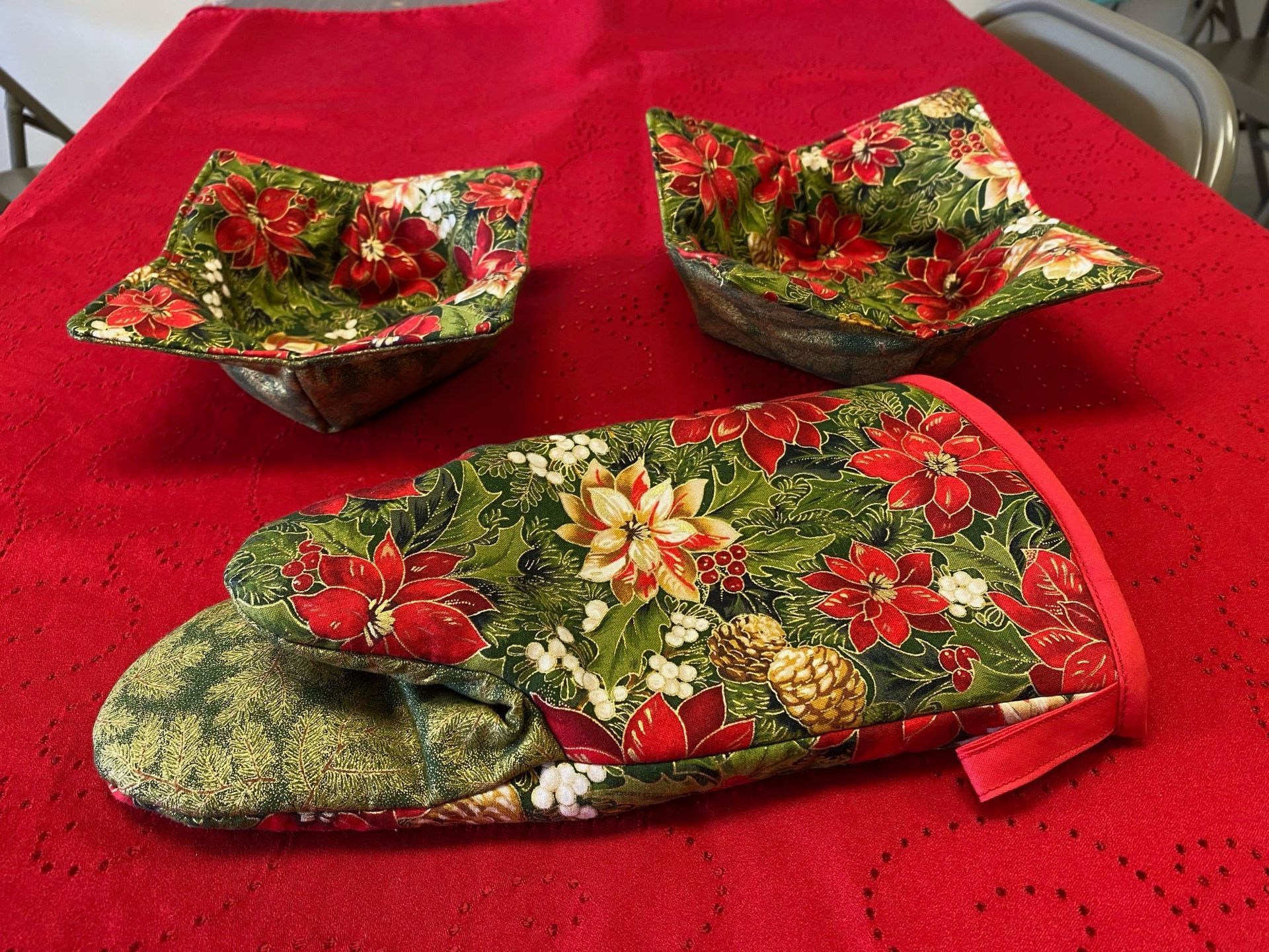 Red floral quilted oven mitt and two matching pot holders on a red textured cloth.