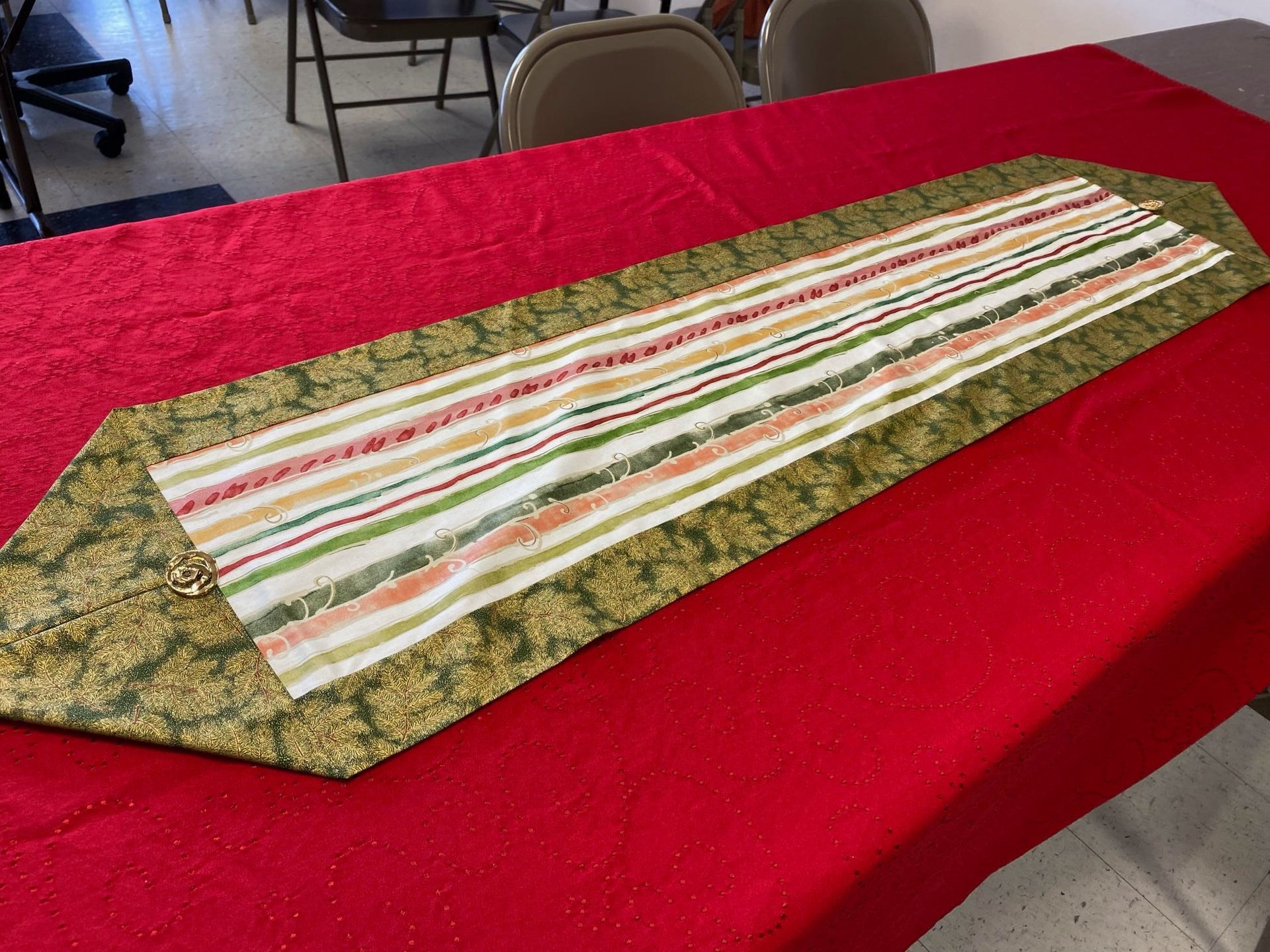 Striped fabric table runner laid diagonally on a red tablecloth in a room with chairs in the background