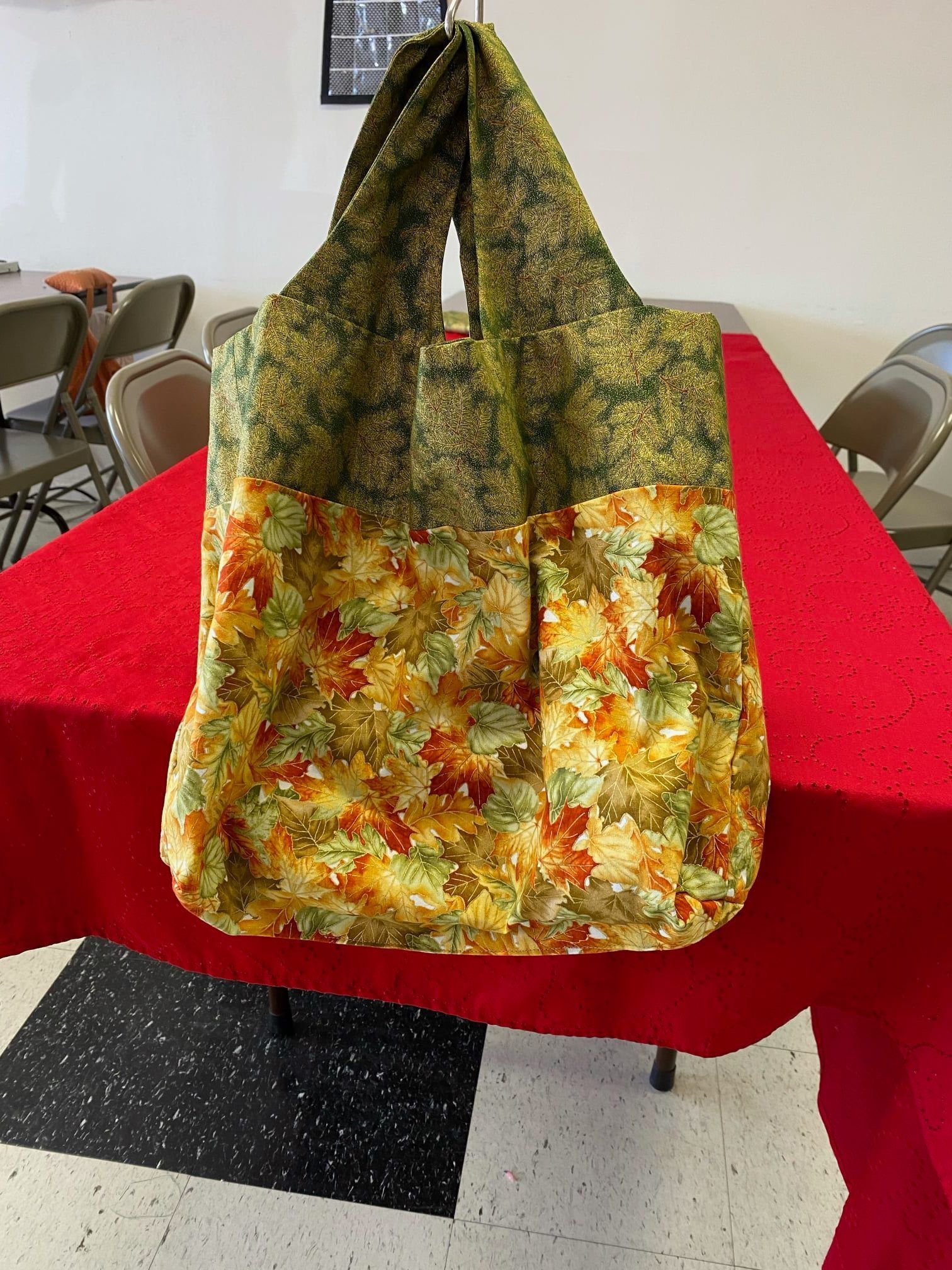Tote bag with green and orange floral pattern hanging over a red table in a dining room